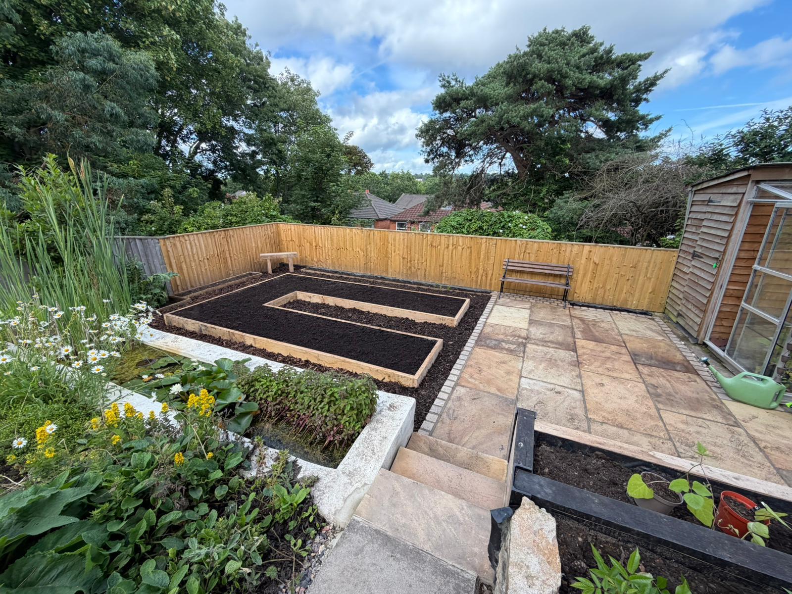 The finished kitchen garden: oak-edged raised beds, sandstone patio and pond, seen from the top of the slope