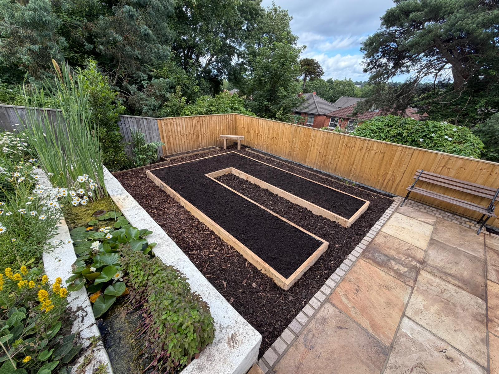 Level raised beds, sandstone patio and pond in a finished garden