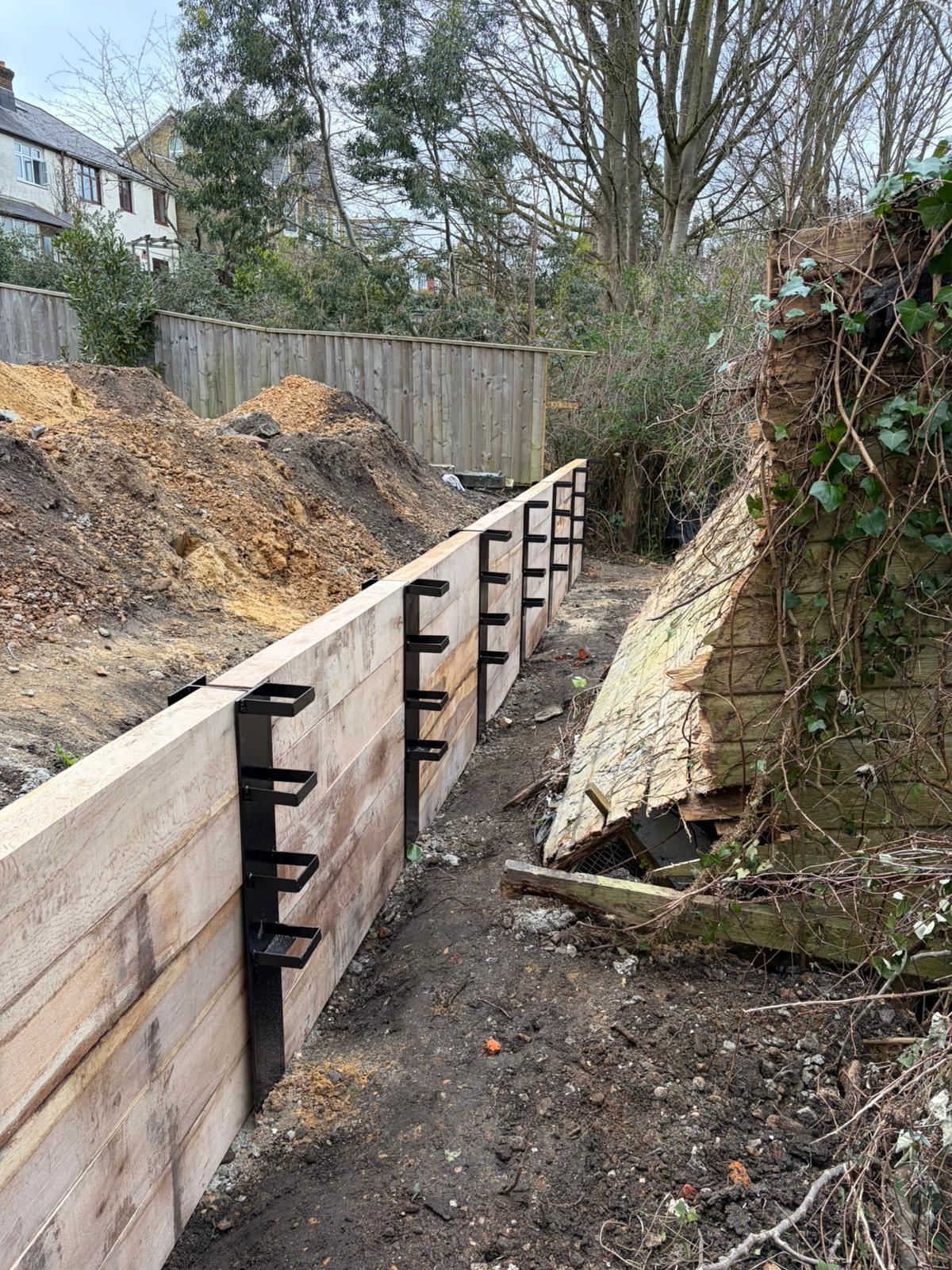 The finished oak sleeper retaining wall with steel brackets, holding back the higher ground